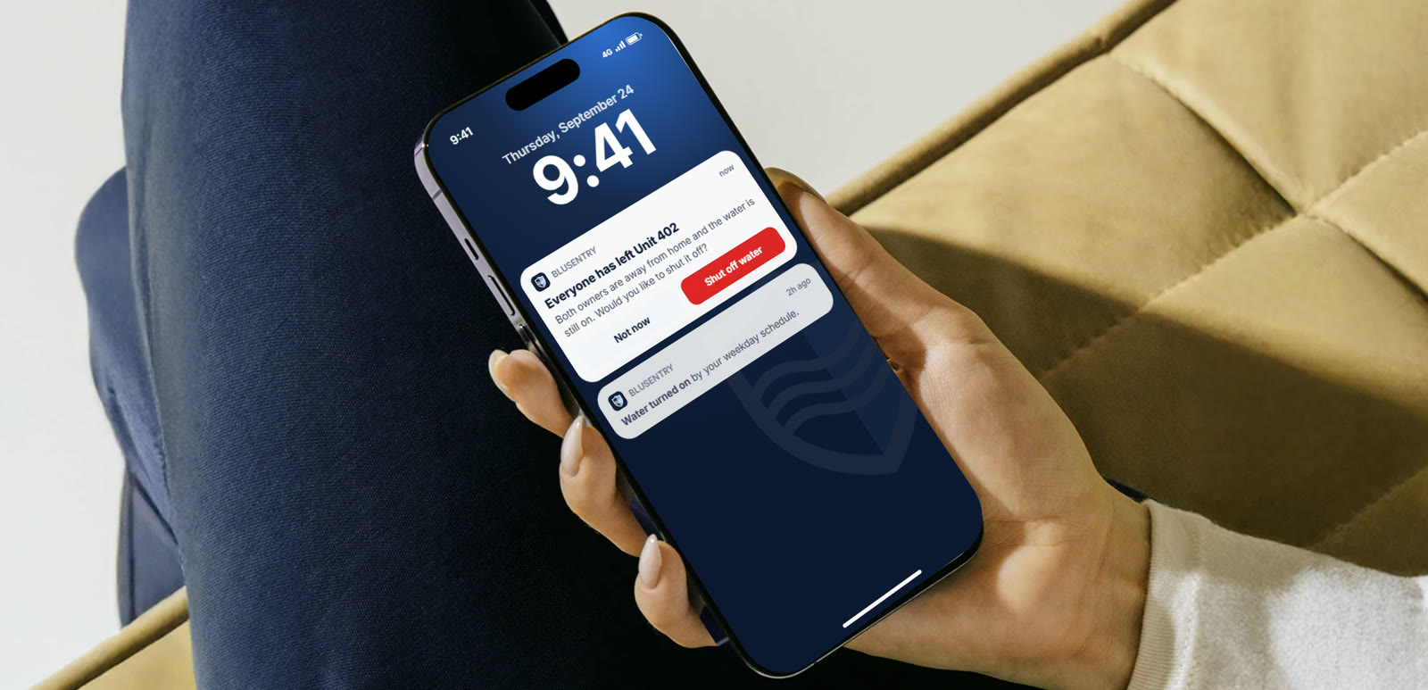 A hand holding a phone showing a BluSentry notification: everyone has left Unit 402 and the water is still on, with a Shut off water button
